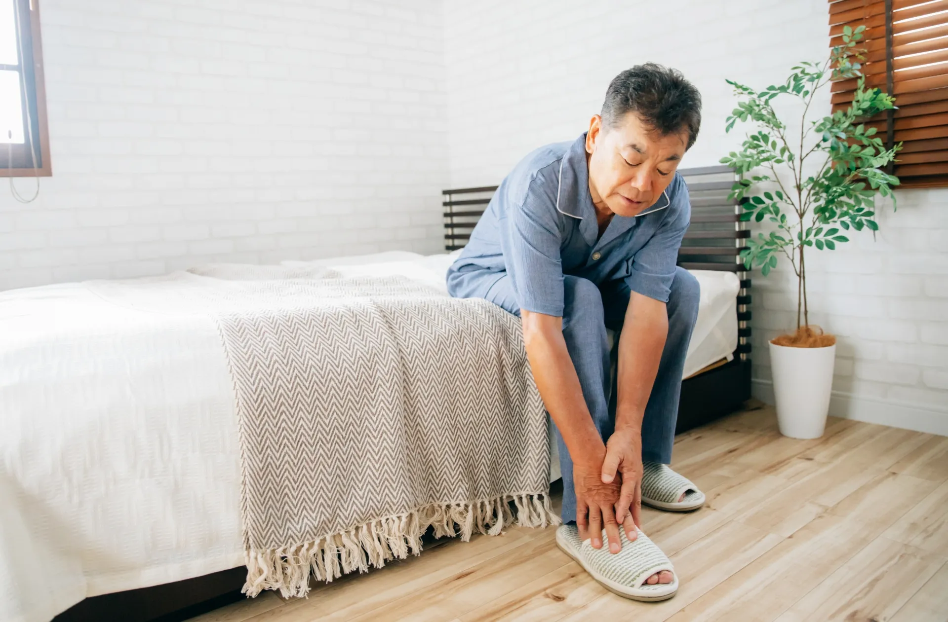 寝起きに冷えを感じて足を揉むシニア男性のイメージ画像