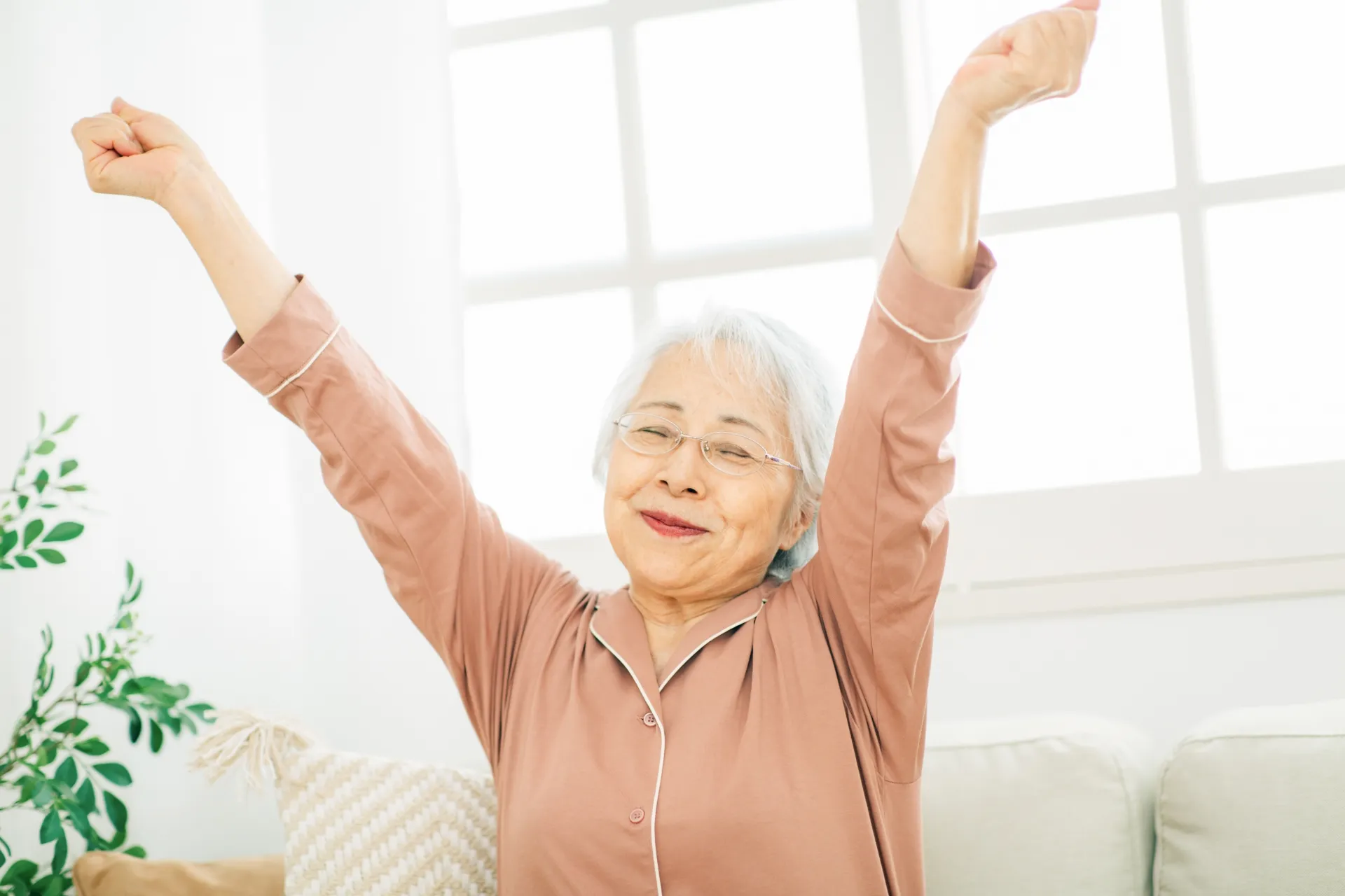 快適な睡眠を取れて元気に伸びをするパジャマのシニア女性のイメージ画像