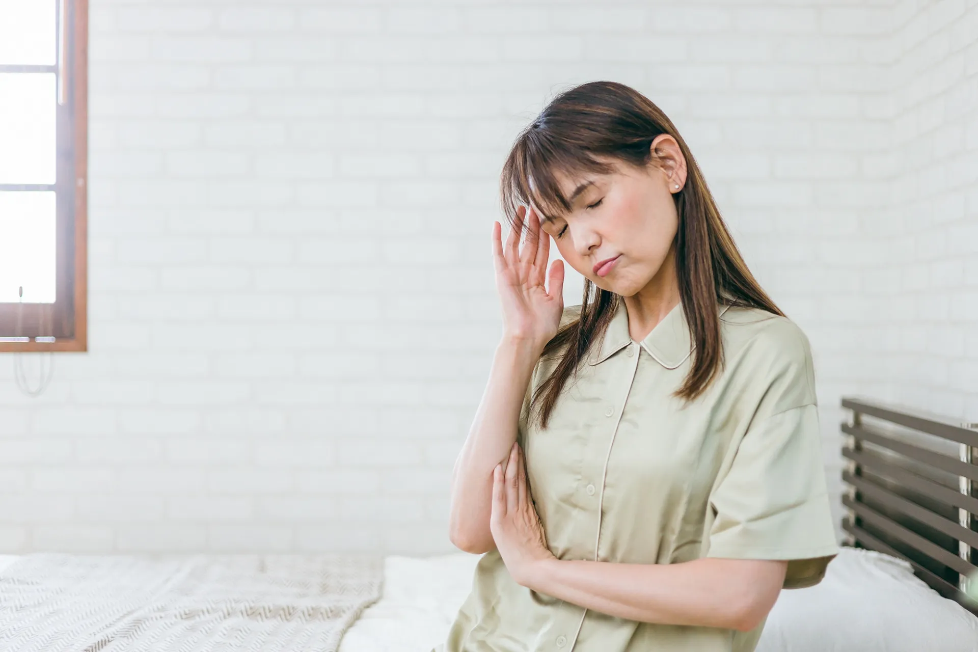 年齢による睡眠の悩みに頭を抑えるミドルシニア女性のイメージ画像