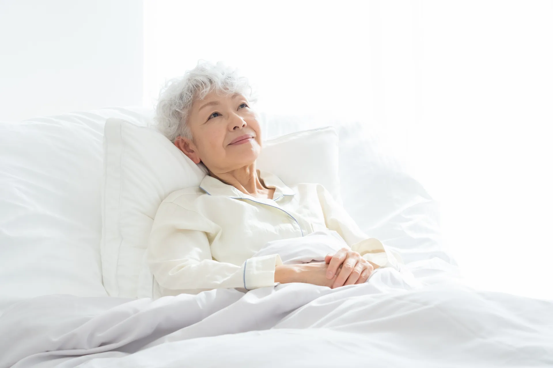 ベッドに横たわるパジャマを着た高齢女性のイメージ画像